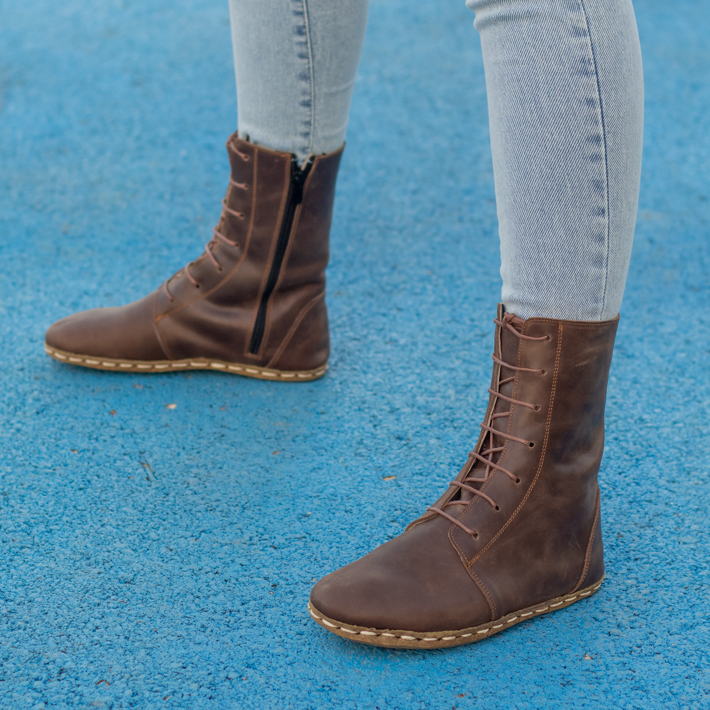 Brown leather barefoot grounding effect boots for women, styled with light jeans on a blue surface.