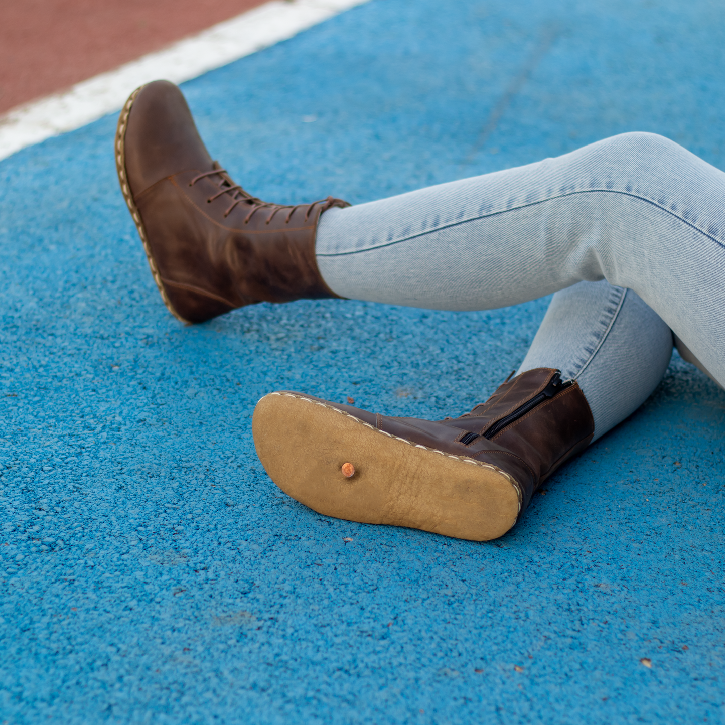Women wearing Barefoot Grounding Effect brown leather boots, showcasing natural movement on blue surface.