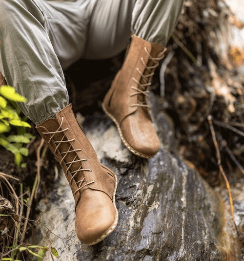 Brown lace-up boots worn by a person sitting on a rock in a natural setting.